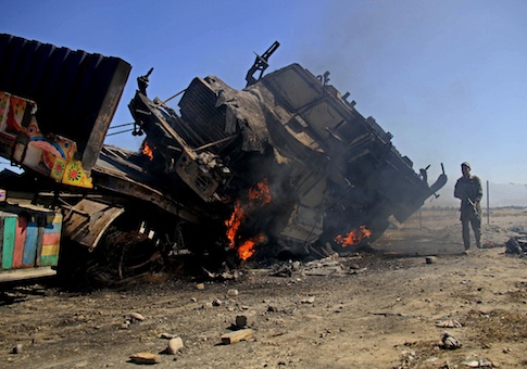 An Afghan policeman stands near a burning NATO supply truck in Behsud district of Jalalabad east of Kabul, Afghanistan