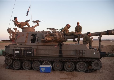 Israeli soldiers are seen on an artillery piece, near the border with the Gaza Strip