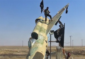 This undated file image posted by the Raqqa Media Center, in Islamic State group-held territory, on Wednesday, Aug. 27, 2014, which has been verified and is consistent with other AP reporting, fighters of the Islamic State wave the group's flag from a damaged display of a government fighter jet following the battle for the Tabqa air base, in Raqqa, Syria