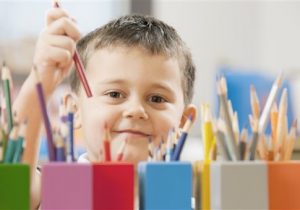 Child picking up a colored pencil (Photo by: Tetra Images/AP Images)
