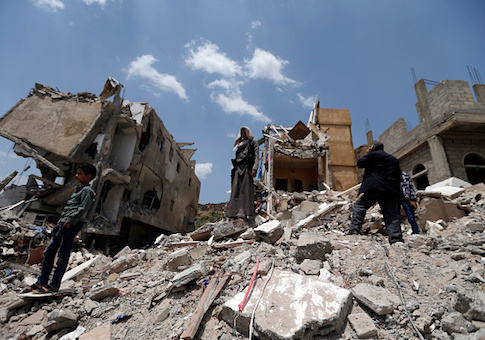 Yemeni men stand on the debris of a house, hit in an air strike on a residential district, in the capital Sanaa