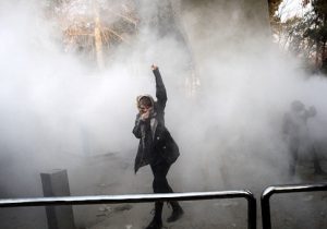 An Iranian woman raises her fist amid the smoke of tear gas at the University of Tehran during a protest driven by anger over economic problems / Getty Images