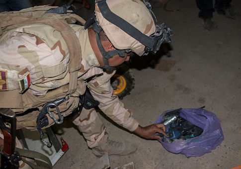 An Iraqi Army soldier inspects a bag of electronic components in a drone and IED factory