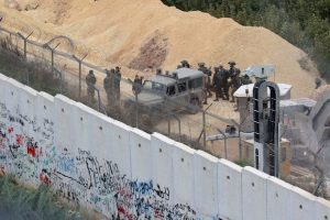 Israeli soldiers gathering by an army vehicle across the concrete Lebanon-Israel border wall near the site of an Israeli excavation site