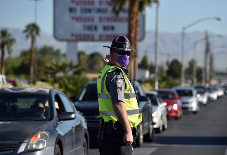 A Nevada Highway Patrol officer directs vehicles as they wait to get into a drive-thru food distributing site